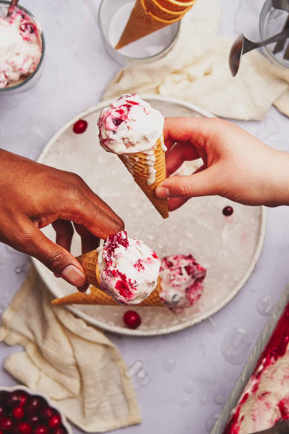 black man and a white woman holding two ice cream cones with cranberry ice cream inside. 