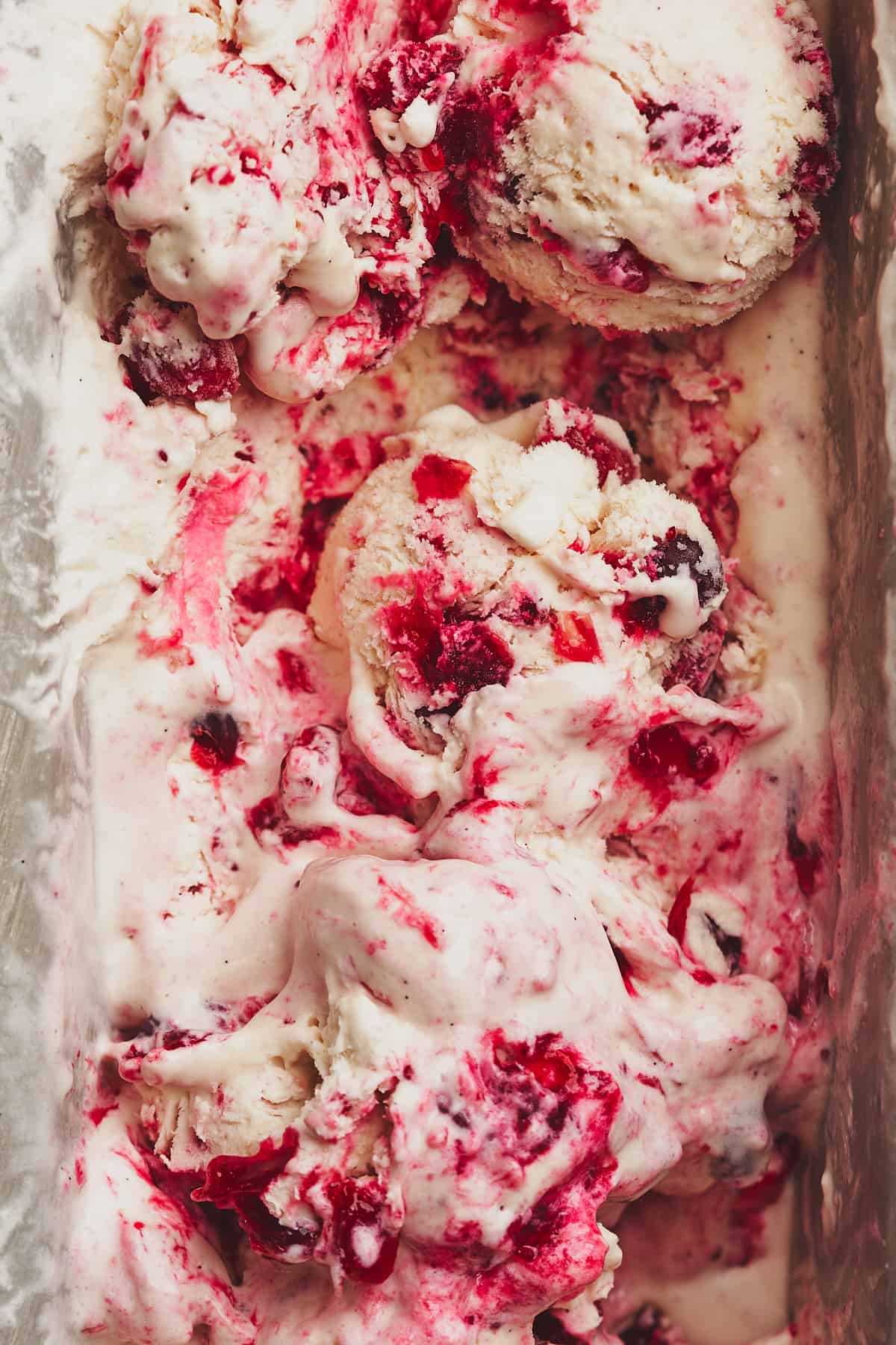 close up shot of cranberry ice cream in a loaf pan rolled into scoops. 