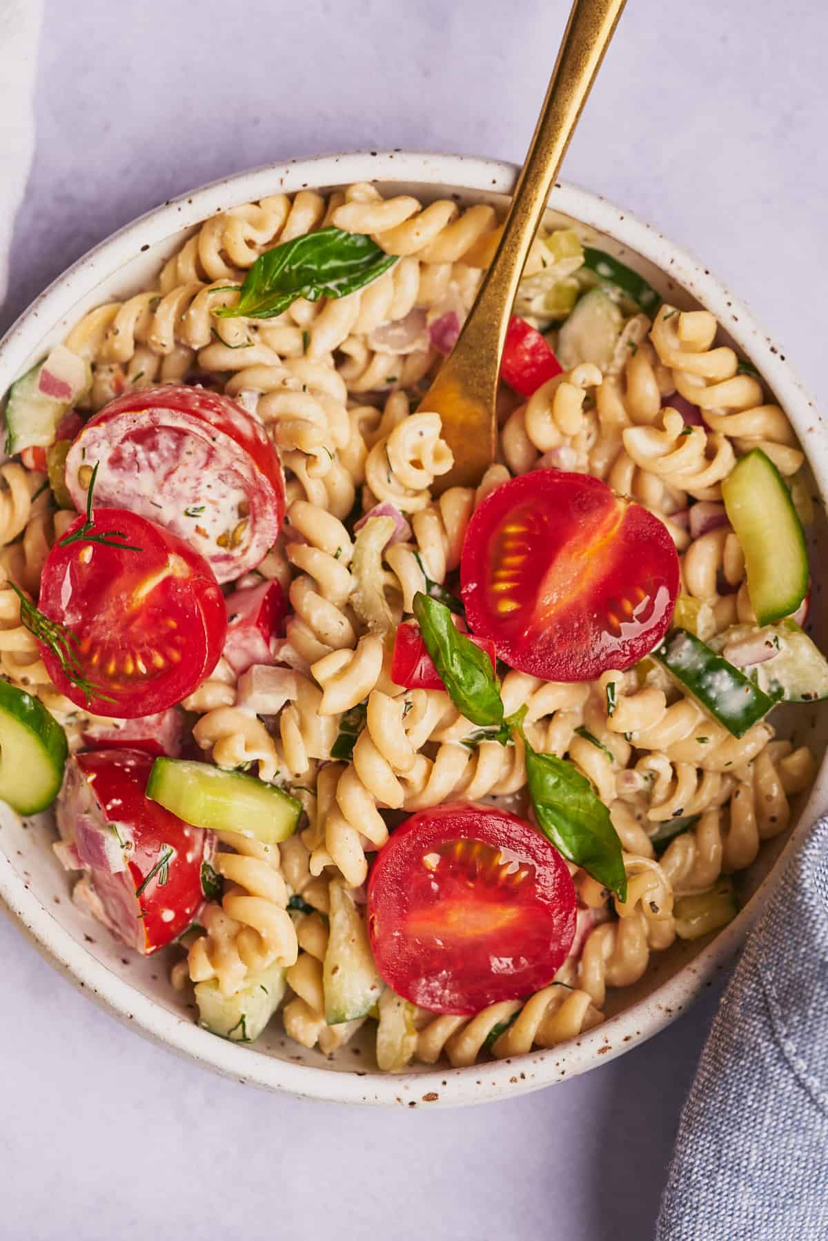 shot of creamy pasta salad in a white ceramic shallow bowl. topped with fresh tomatoes and basil. 