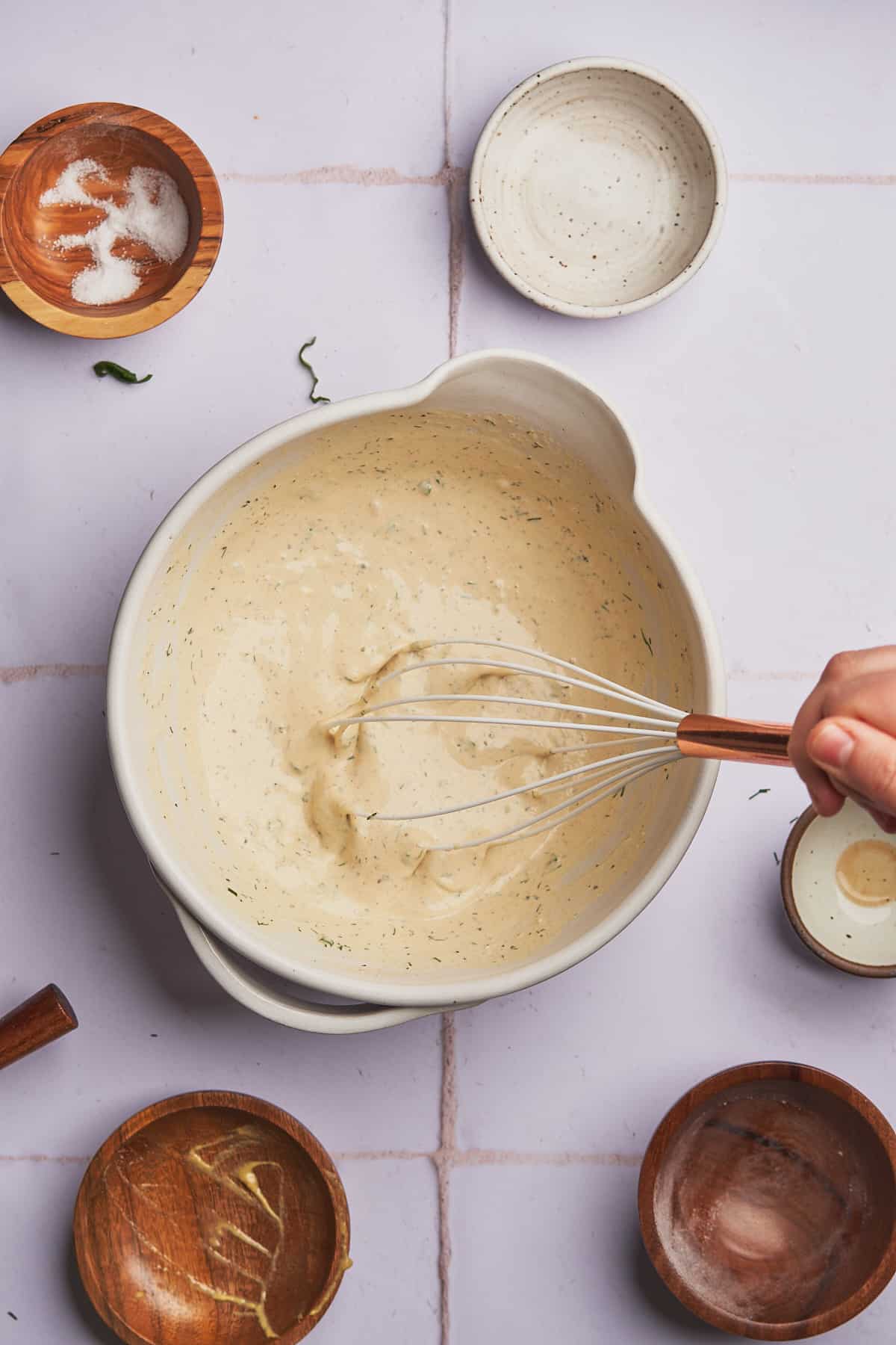 hand whisking together creamy salad dressing in a mixing bowl. 