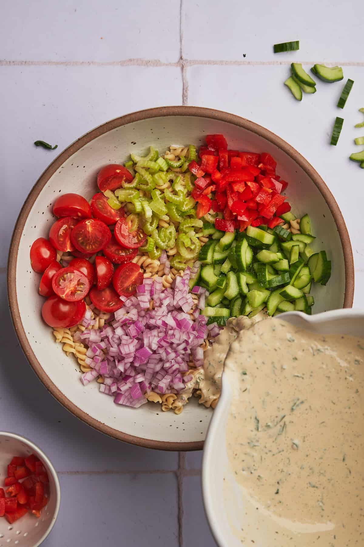 pouring salad dressing onto pasta salad and vegetables.