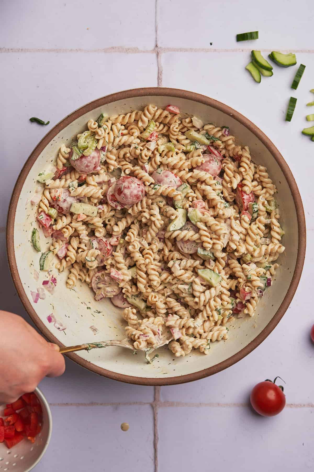 hand using a spoon to mix pasta and vegetables together with a creamy sauce. 