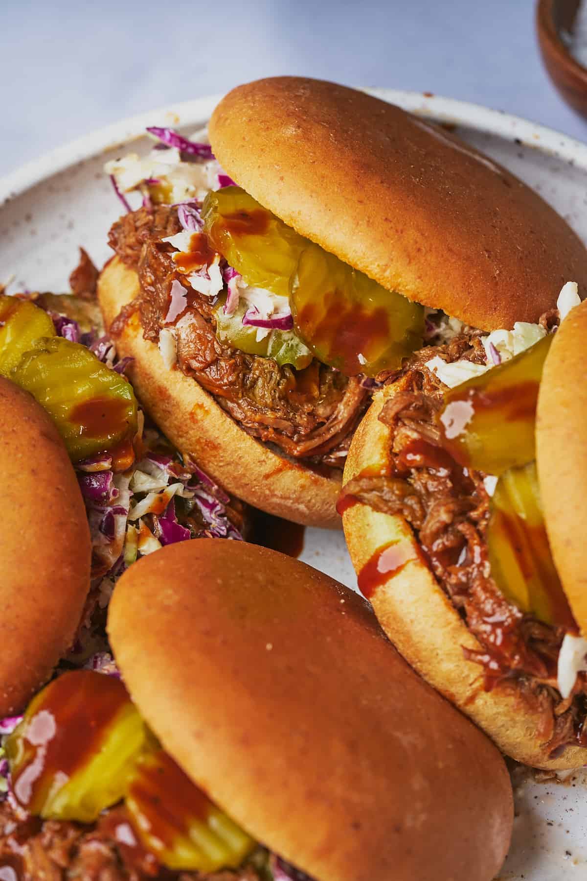 close up shot of dutch oven pulled pork on a bun with bbq sauce, coleslaw and pickles.