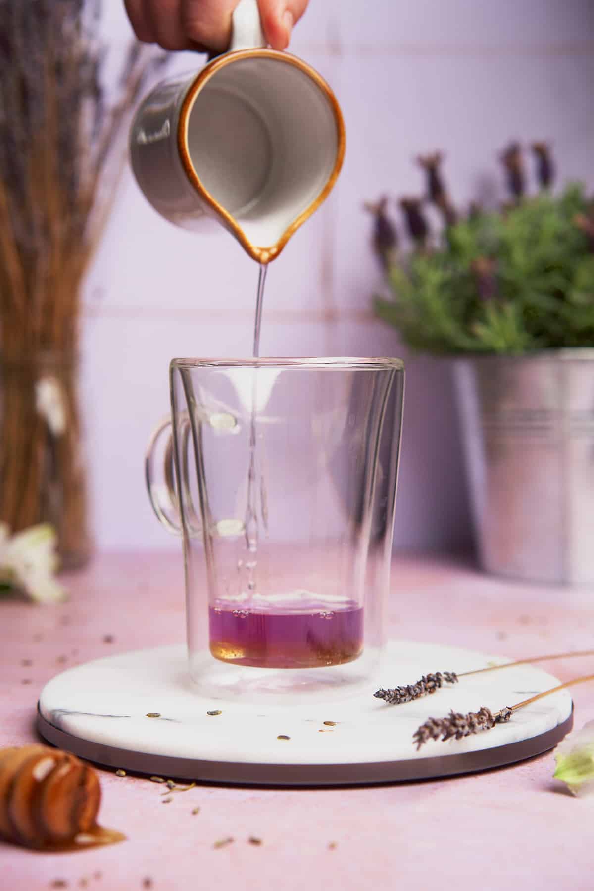 pouring lavender simple syrup into a glass coffee mug with honey in it. 
