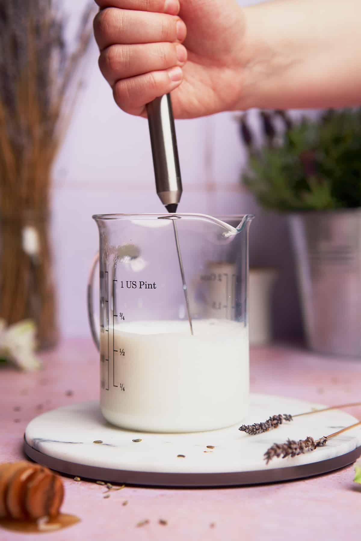 frothing hot milk in a glass beaker with a hand frother. 