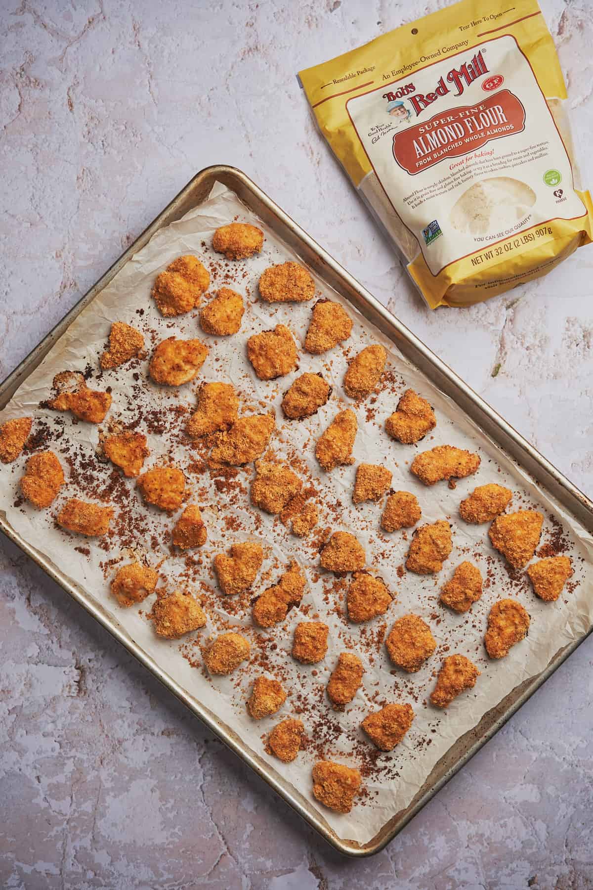 baked chicken nuggets on a baking sheet next to a bag of bob's red mill almond flour
