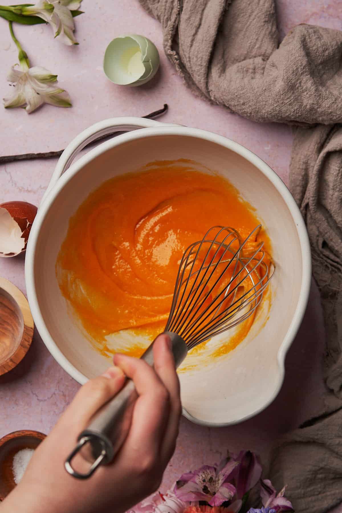 hand whisking together bright orange egg yolks, and sweetener in a bowl. 