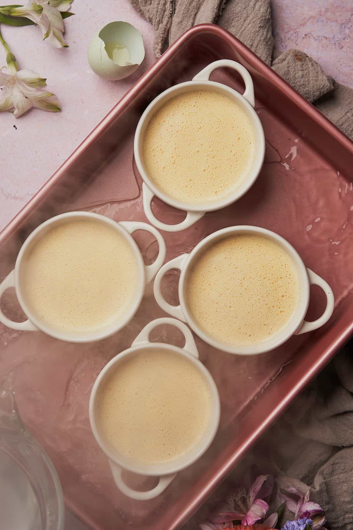 pouring boiling water into a baking pan with ramekins with egg custard in them. 