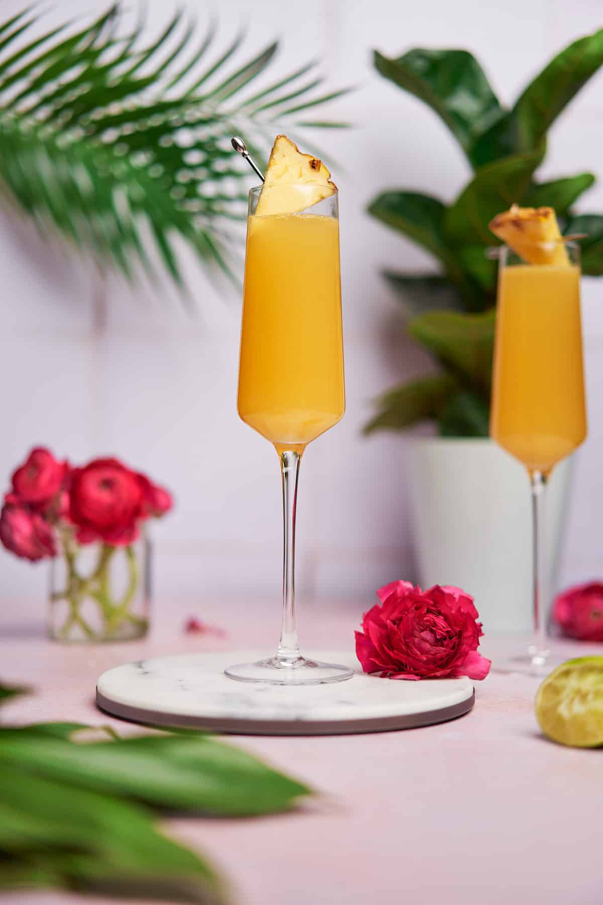 pineapple mimosas, surrounded by lots of green tropical plants, and bright pink flowers. 