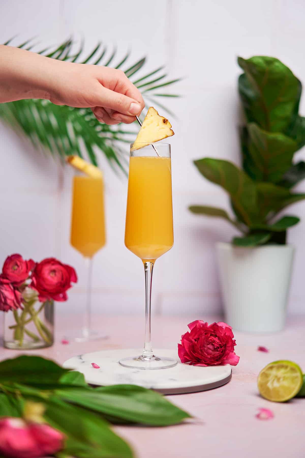 hand gently placing on a cocktail pic with a wedge of pineapple on it on top of a pineapple mimosa.