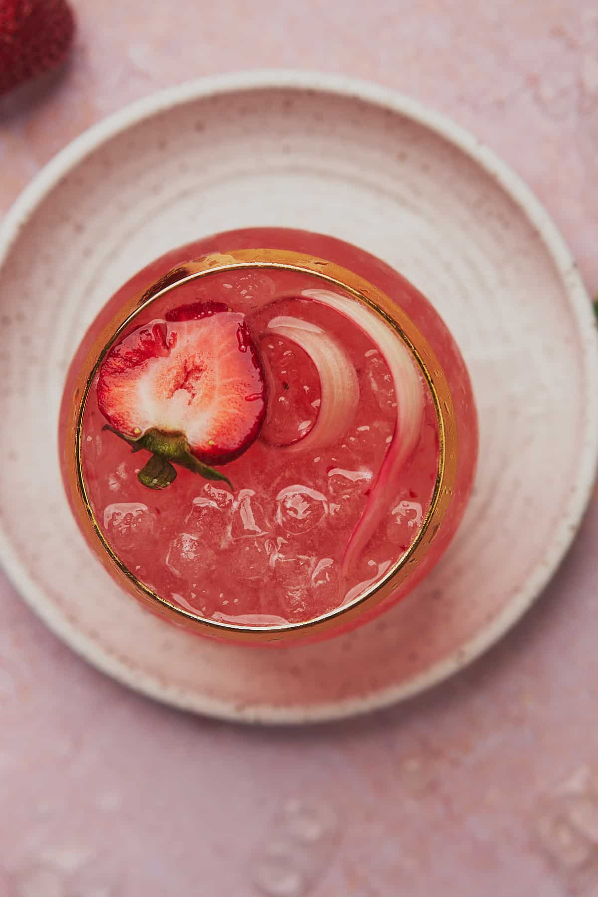 overhead view of a rhubarb gin cocktail, garnished with fresh strawberry and rhubarb. 