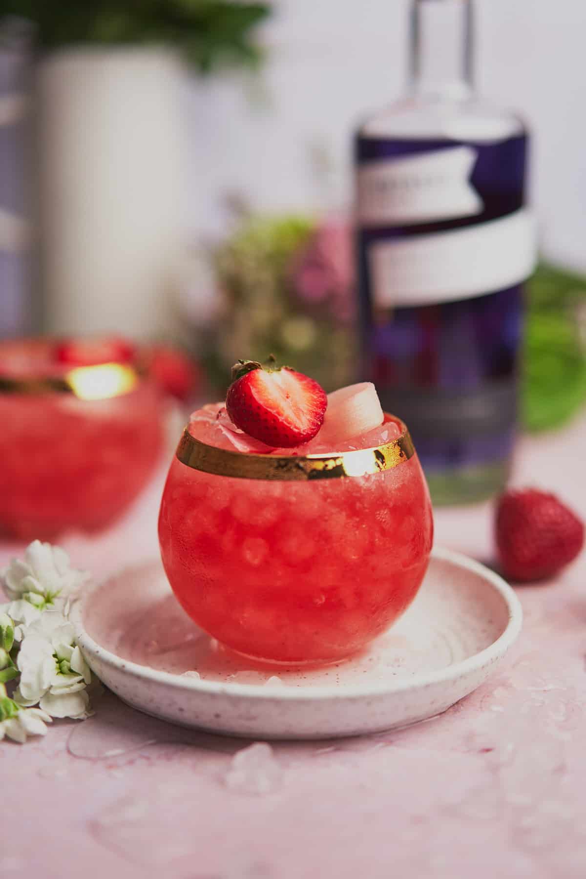 stunning straight on shot of a rhubarb gin cocktail with strawberries and empress gin in the background. 