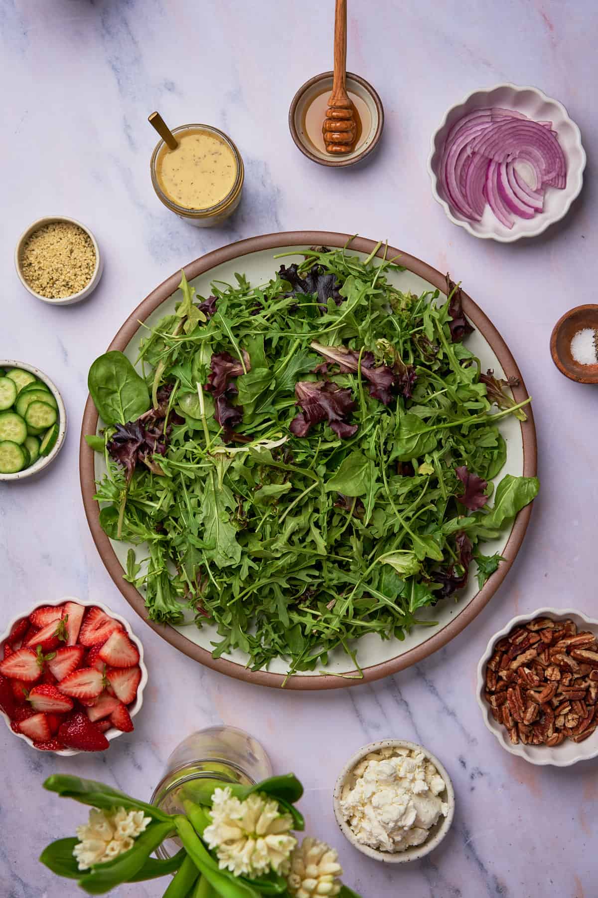 base of spring mix and arugula on a serving platter surrounding by other ingredients to make a strawberry goat cheese salad. 