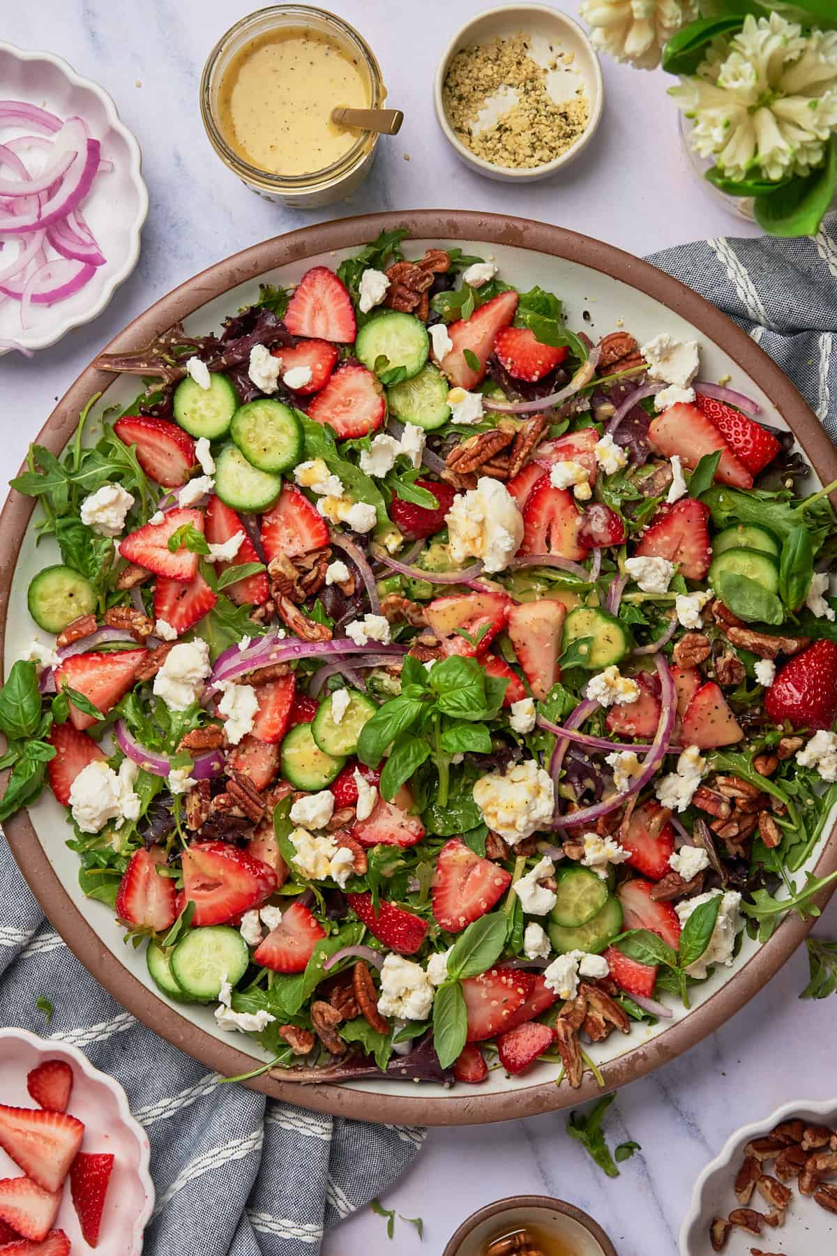 bright and colorful strawberry goat cheese salad with red onions, cucumbers, fresh strawberries, basil, goat cheese, and pecans.