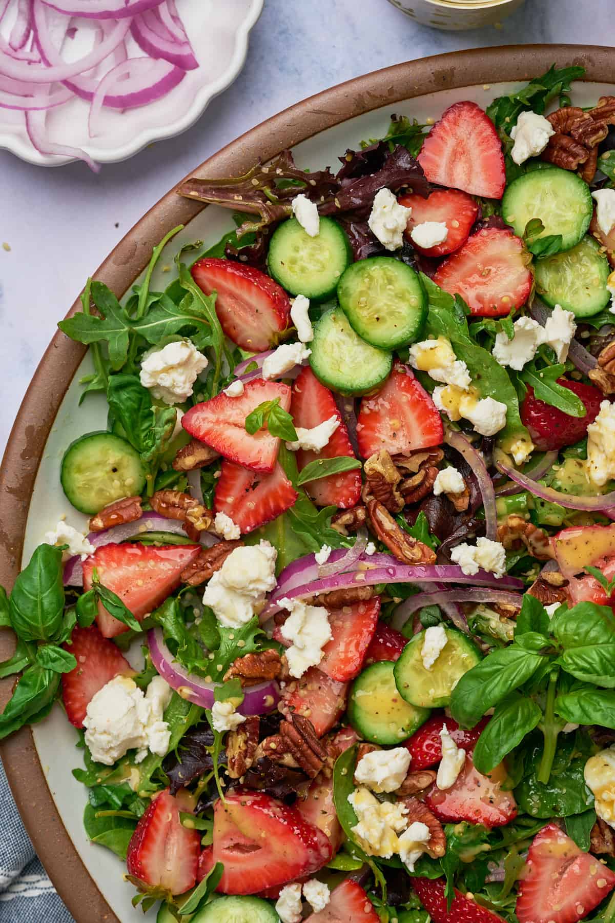 close up shot of a strawberry goat cheese salad with cucumbers, pecans, red onions, and basil. 