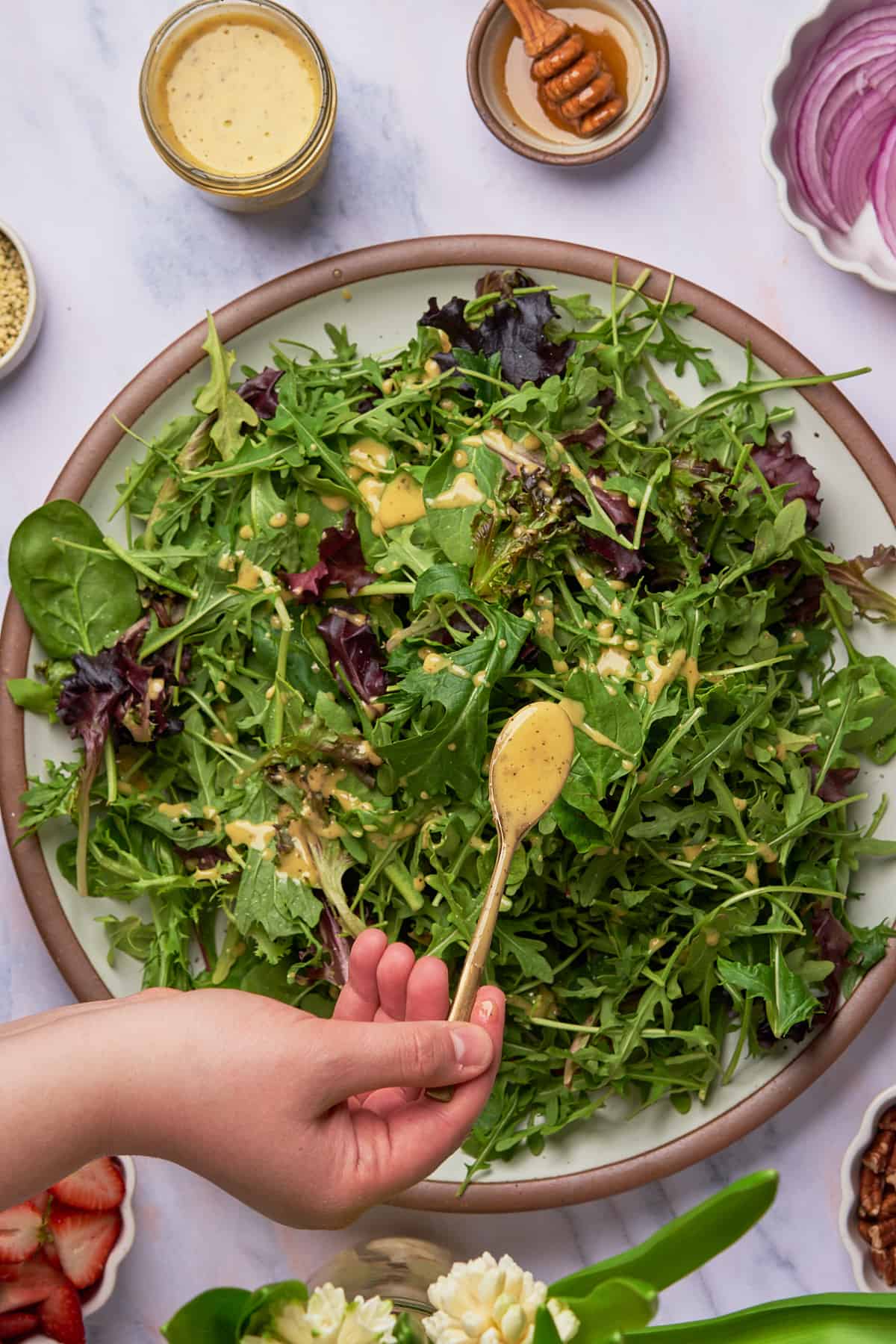 hand pouring salad dressing over top of greens with a spoon.