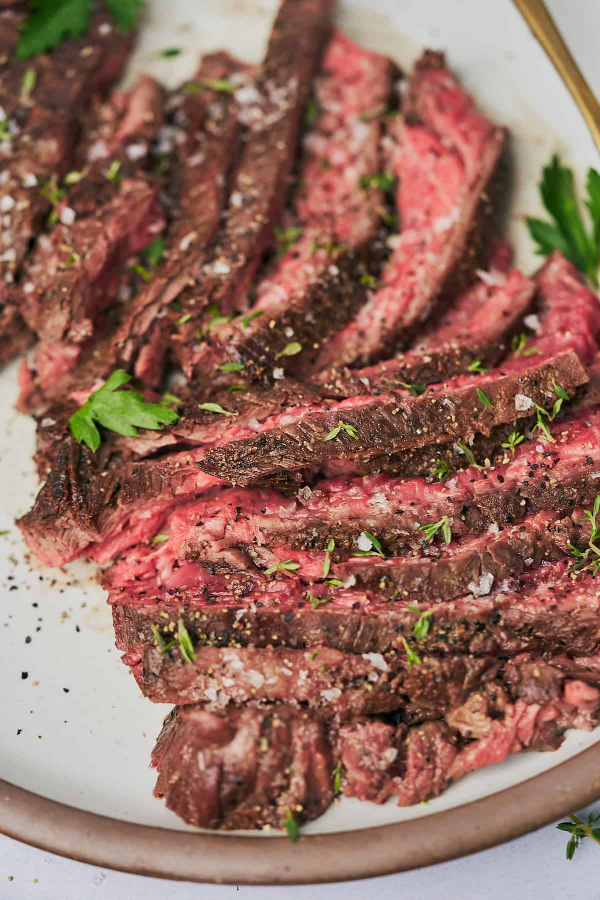 Close up shots of a juicy medium rare steak cut and served on a plate with parsley and flaky salt.