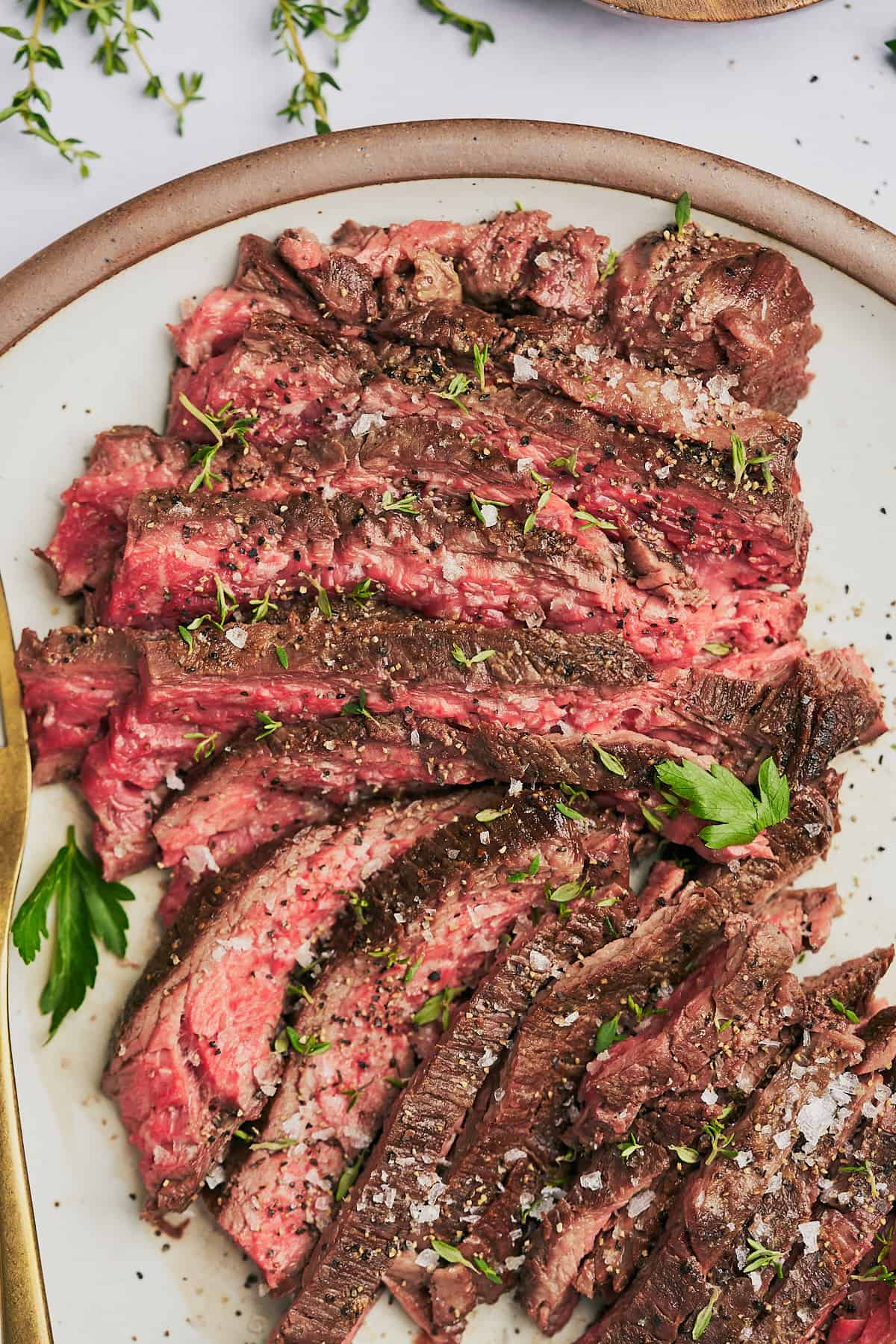 flat lay shot of a delicious medium rare bavette steak, garnished with parsley, thyme, sea salt, and pepper. 