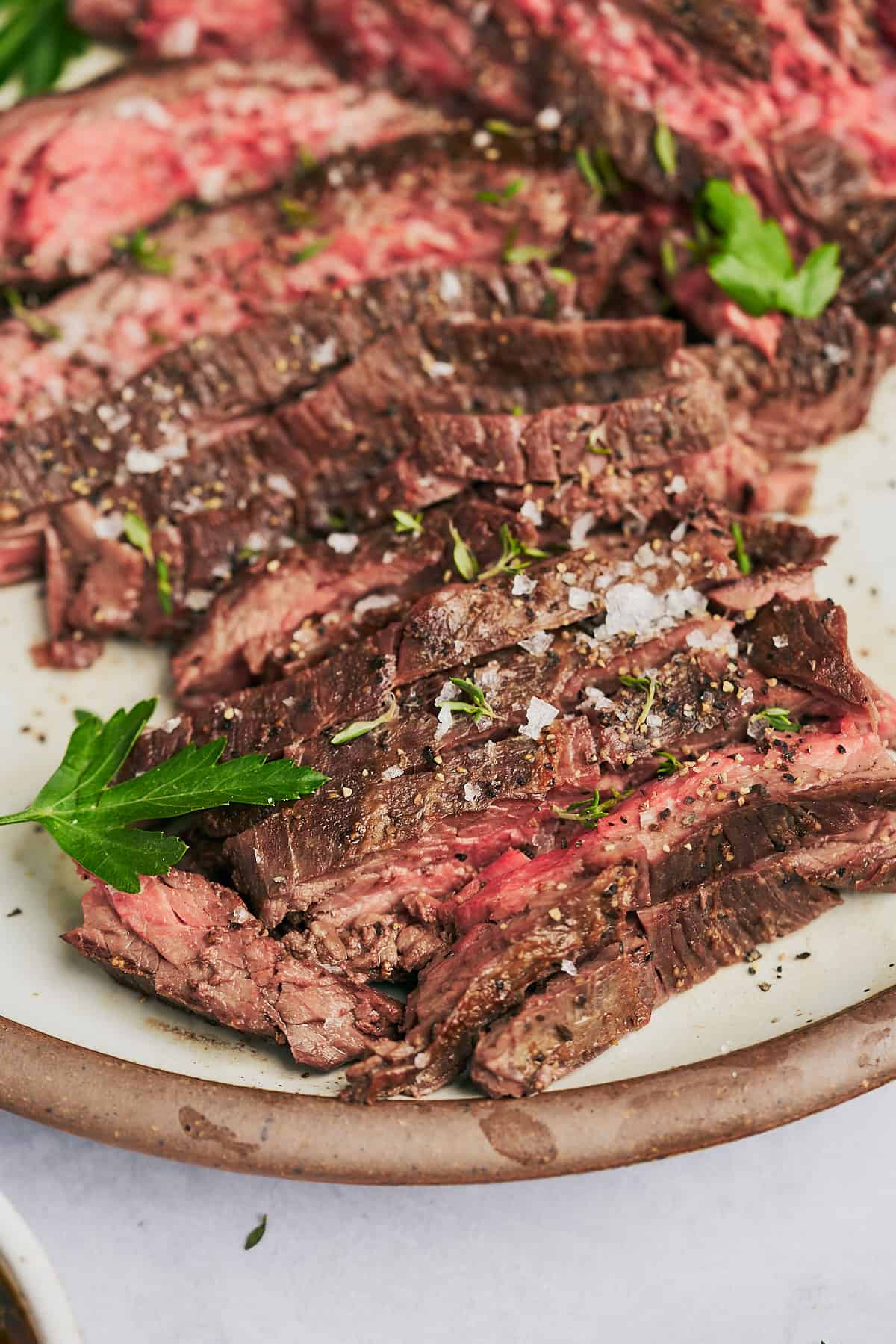 Delicious bavette steak seasoned with parsley, thyme, pepper, and sea salt on a ceramic speckled plate with a brown rim.