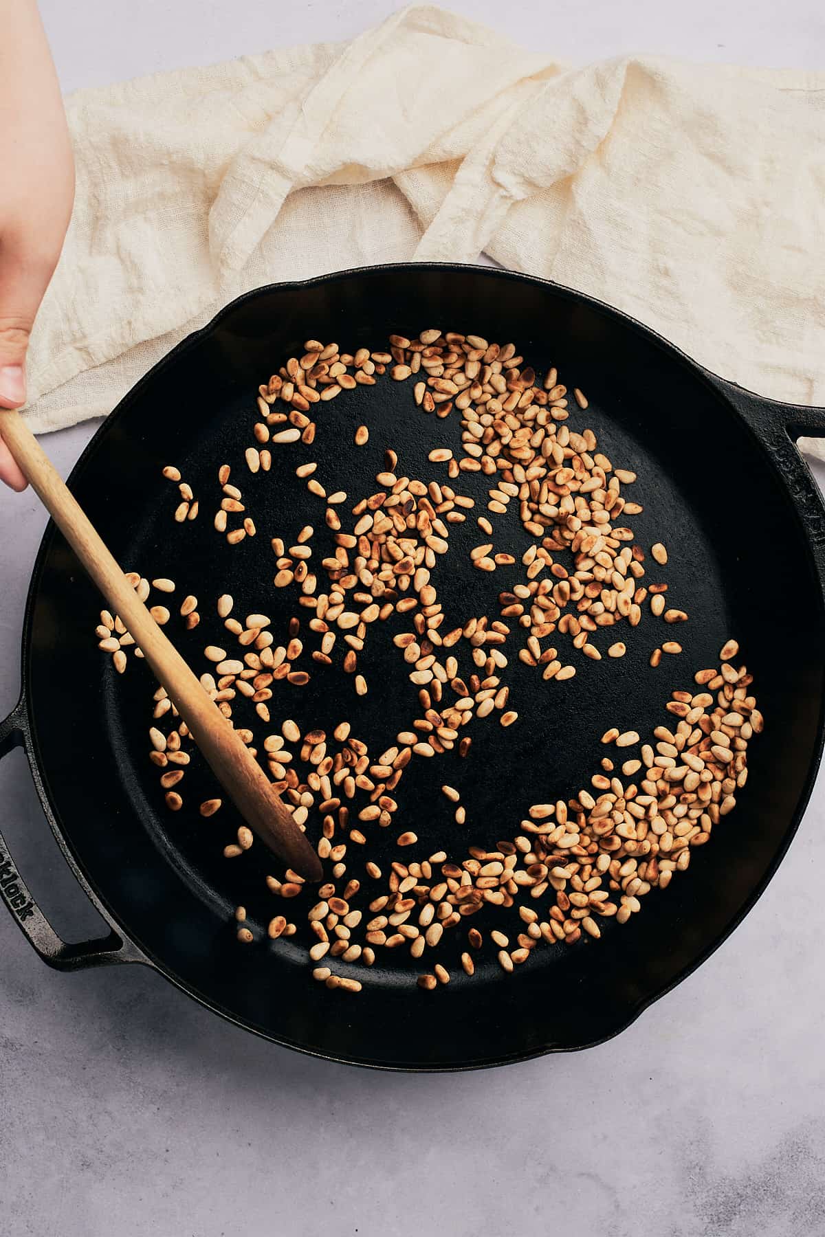 toasty pine nuts in a cast iron skillet being stirred with a wooden spoon.