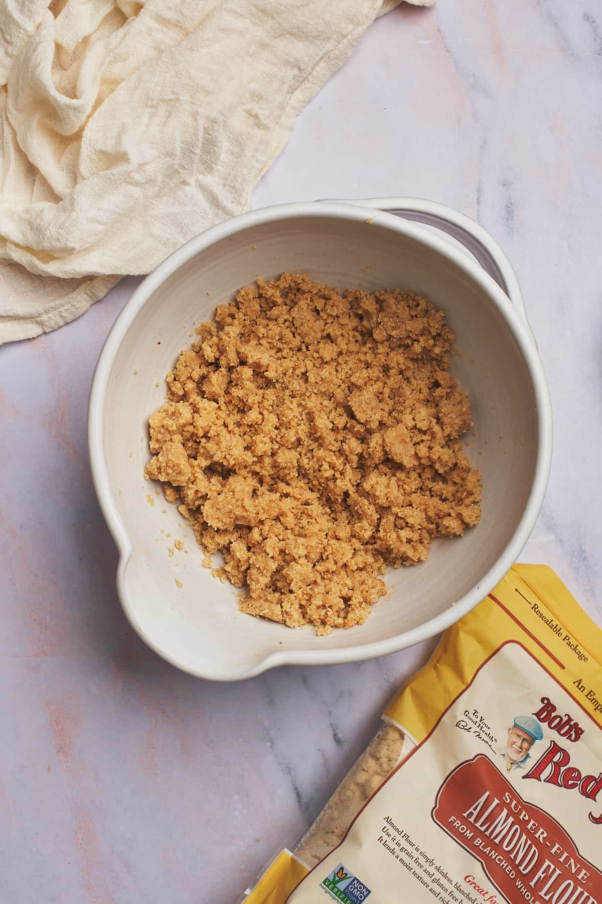 crumbled almond flour, sweetener, and butter mixture in a bowl with a bag of bob's red mill almond flour nearby. 