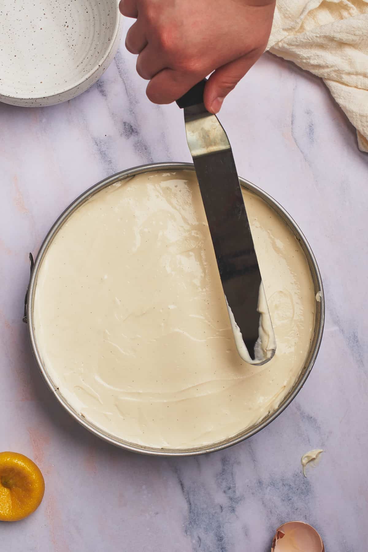 cheesecake filling being spread into a springform pan with an angled spatula. 