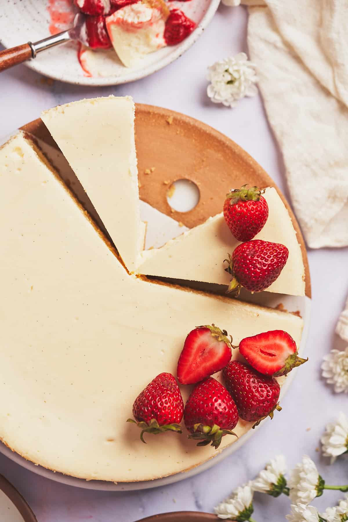 close up shot of a cheesecake cut into pieces and topped with fresh strawberries. 