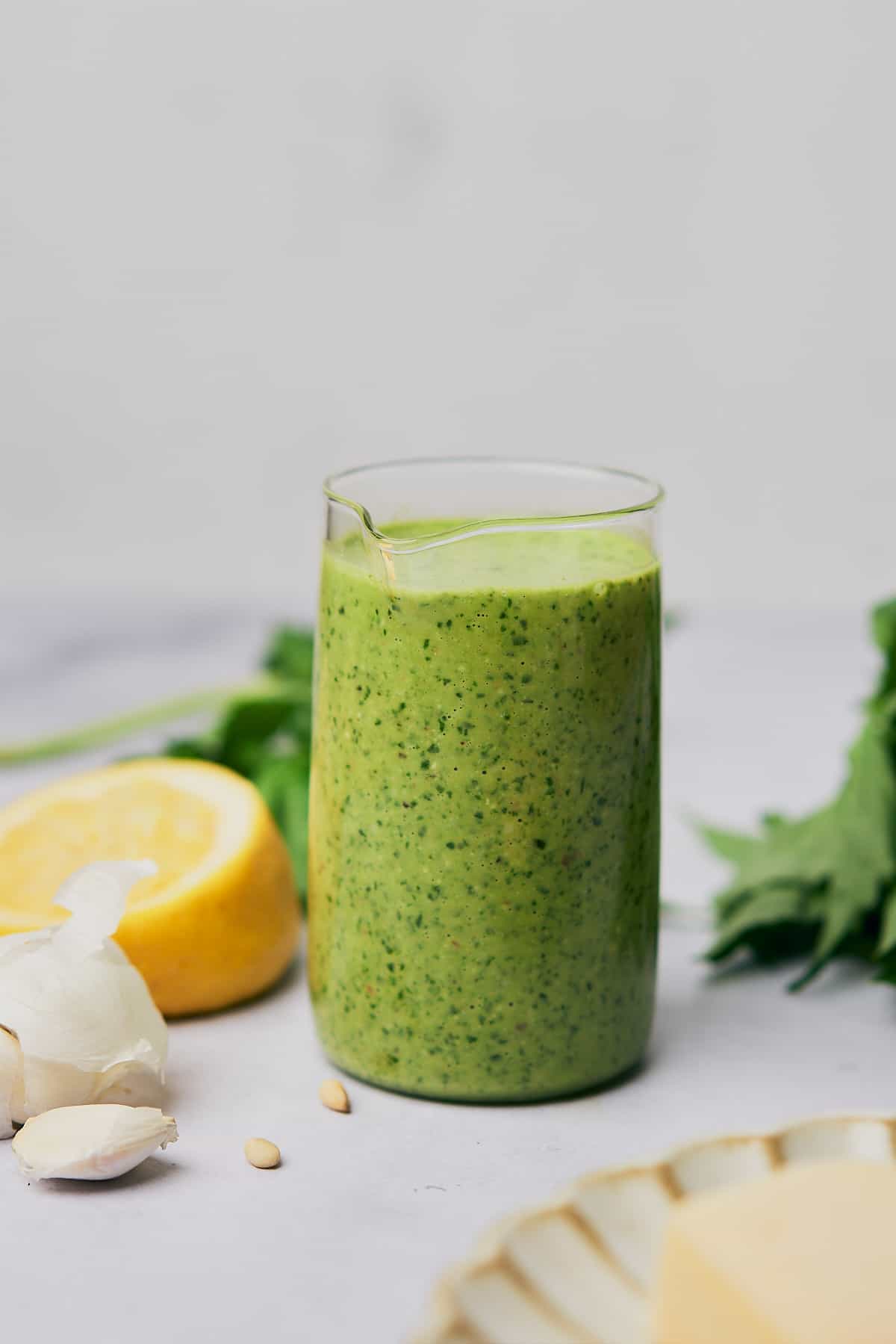 pesto vinaigrette in a glass container, surrounded by fresh basil, garlic, and lemon. 