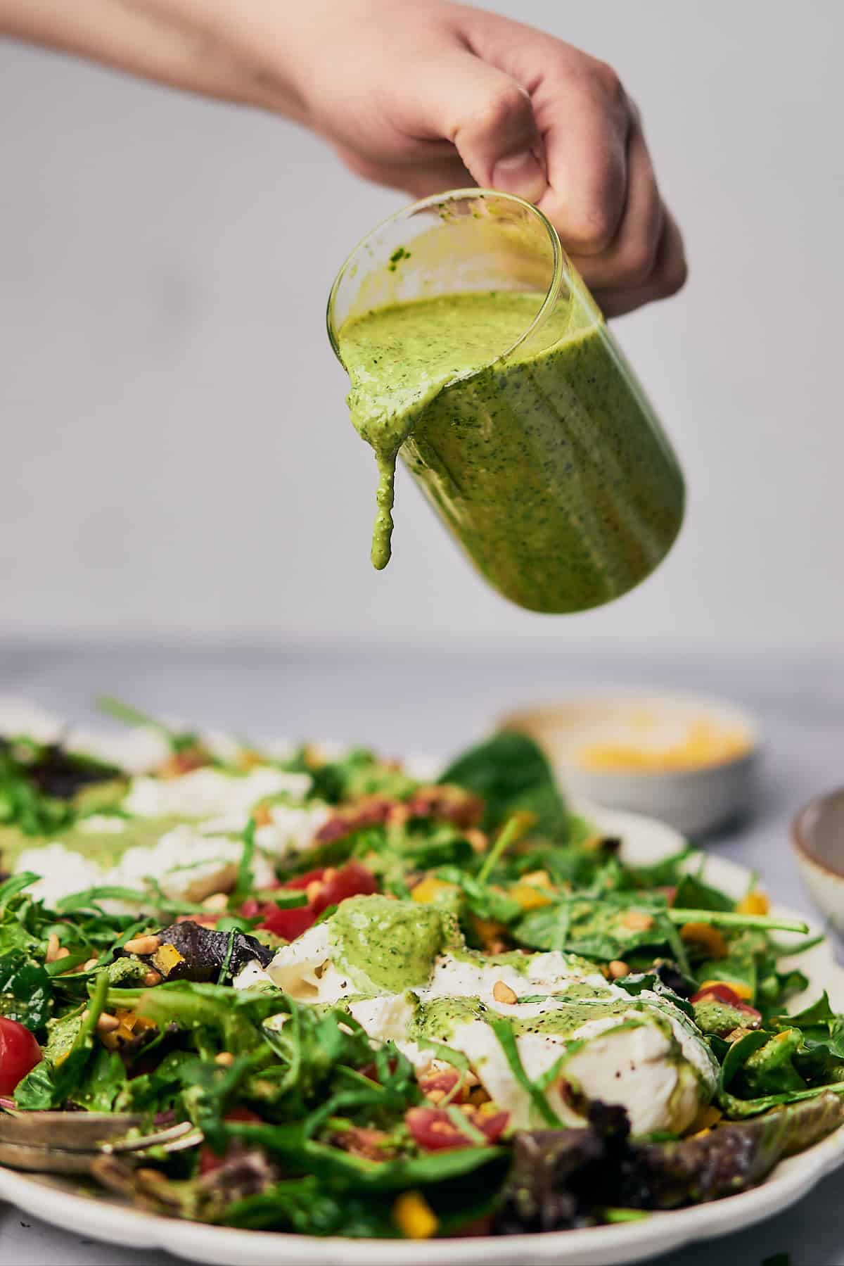 pouring pesto vinaigrette over top of a burrata salad. 