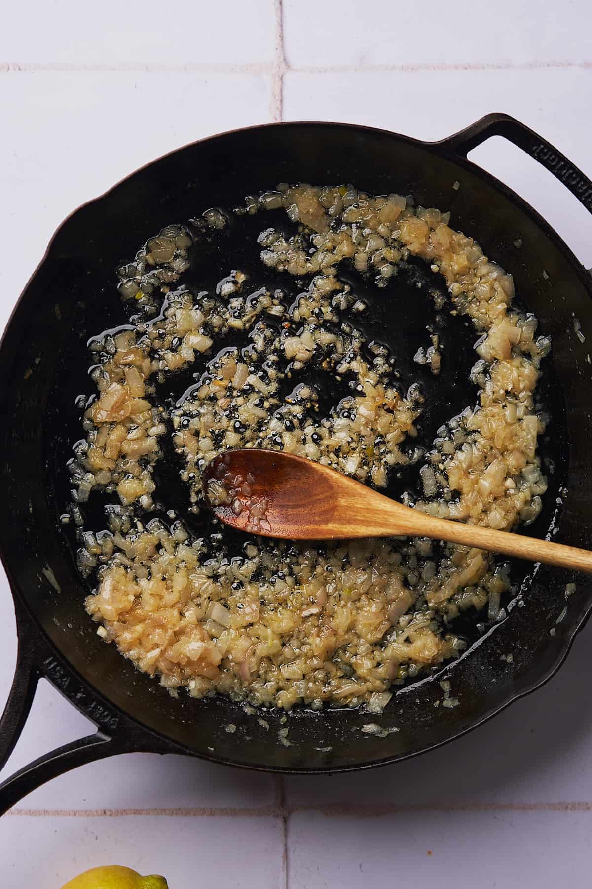 cooked shallots in a skillet with garlic being stirred with a wooden spoon. 