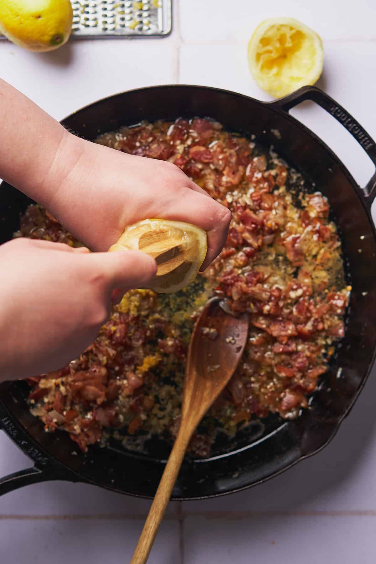 juicing a lemon into a skillet with cooked bacon, shallots, and garlic. 