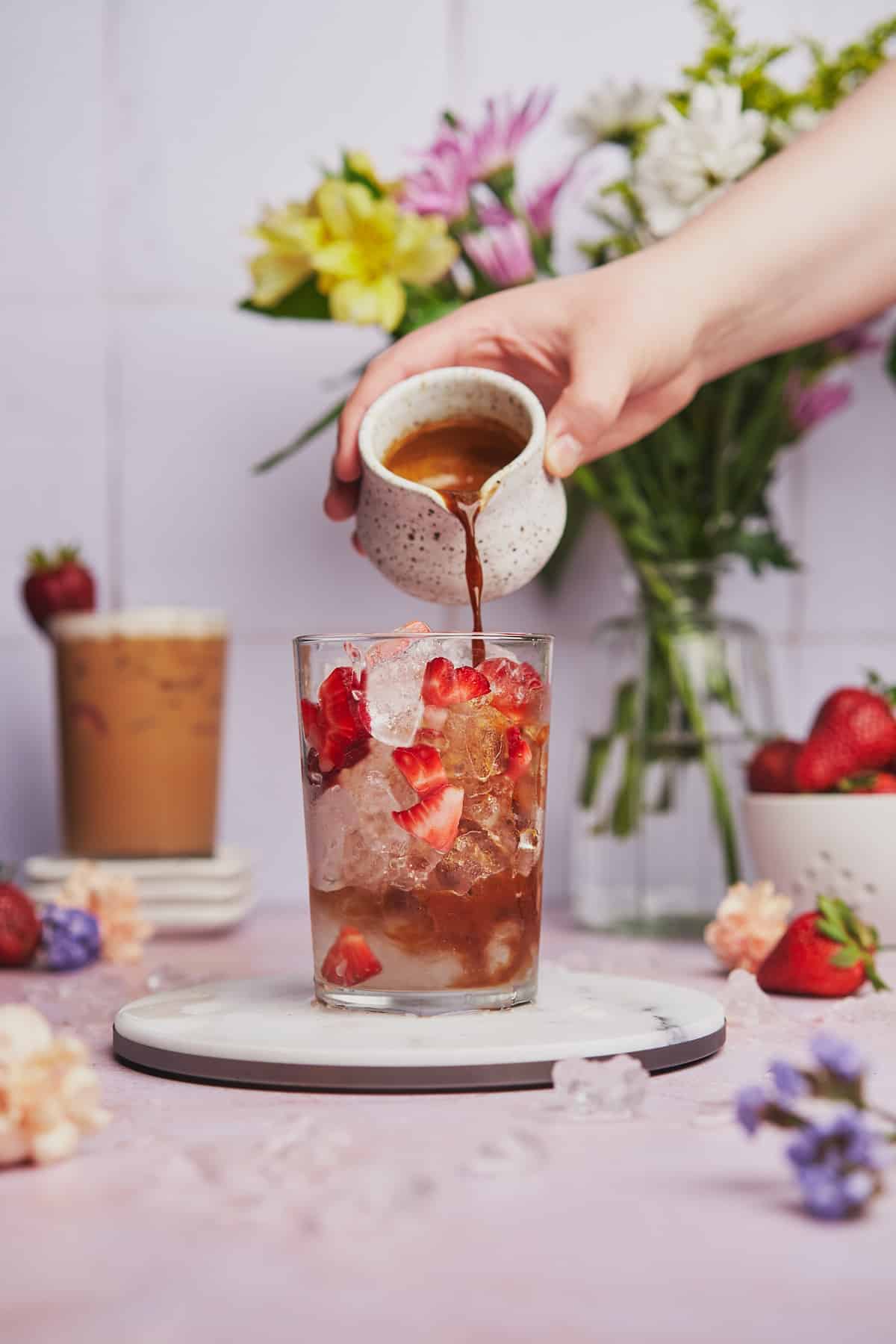 hand pouring espresso into a glass with ice and strawberries.
