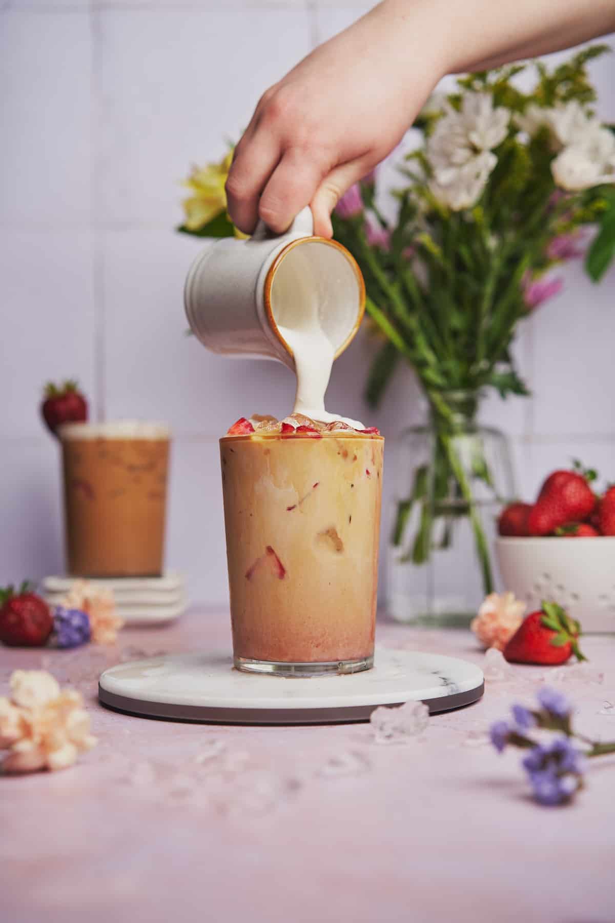 pouring foamy milk and strawberry syrup into a glass. 