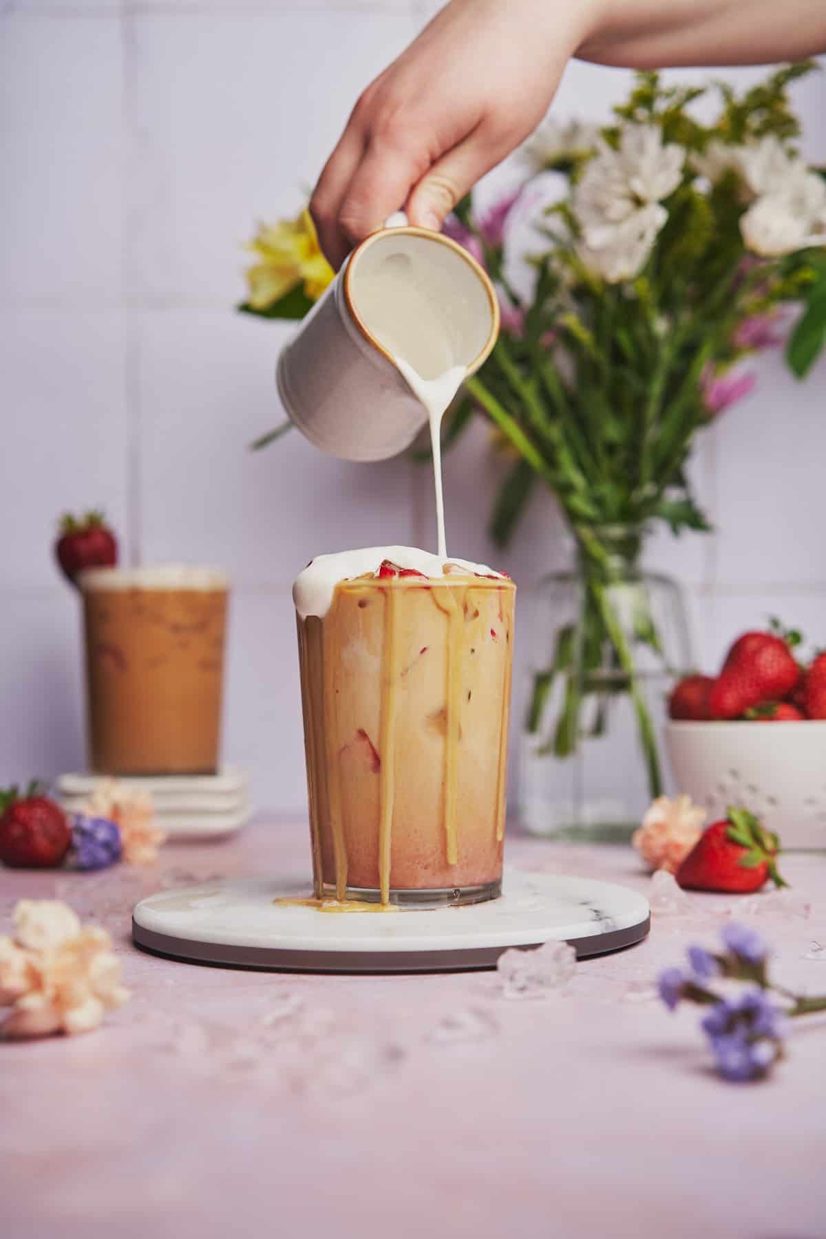 pouring cream to the top of a strawberry latte, with some of the cream pouring down the sides. 