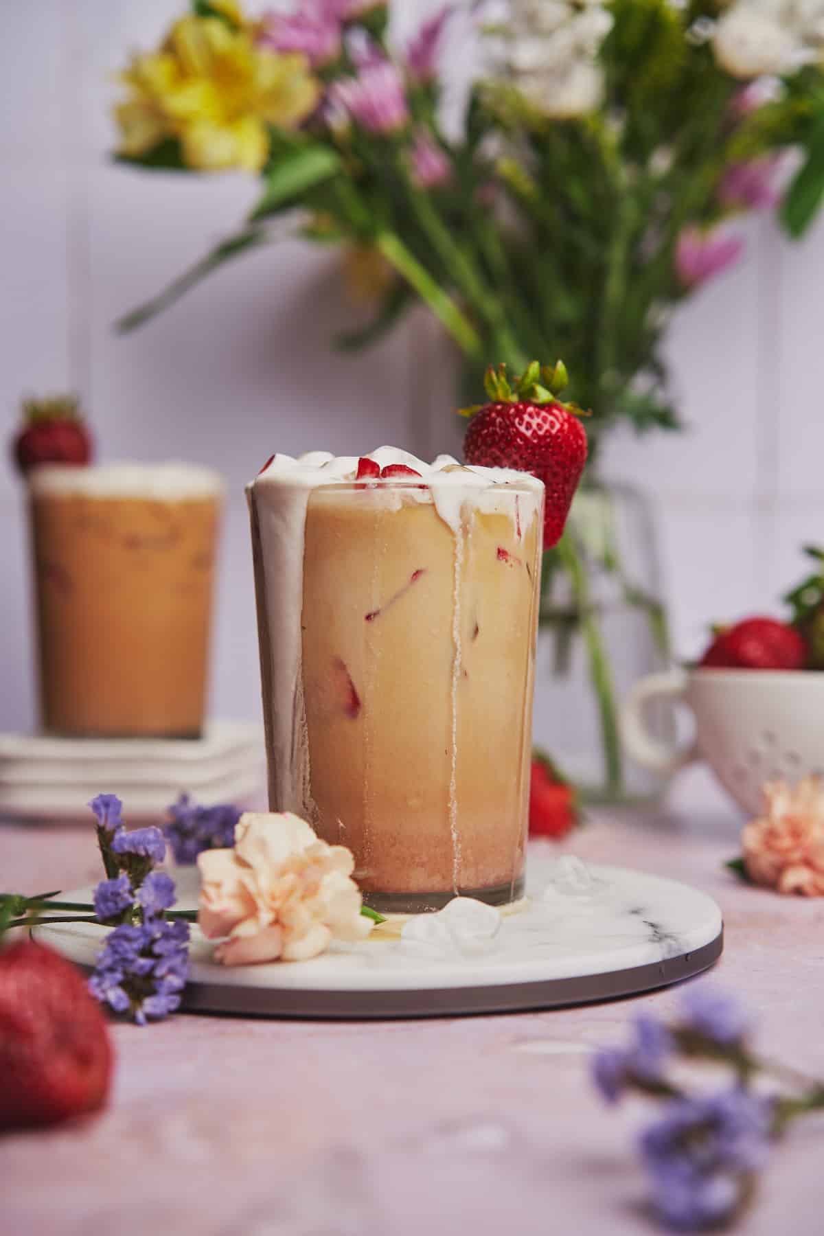 close up shot of a strawberry latte, with cold foam dripping down and lots of fresh strawberries. 