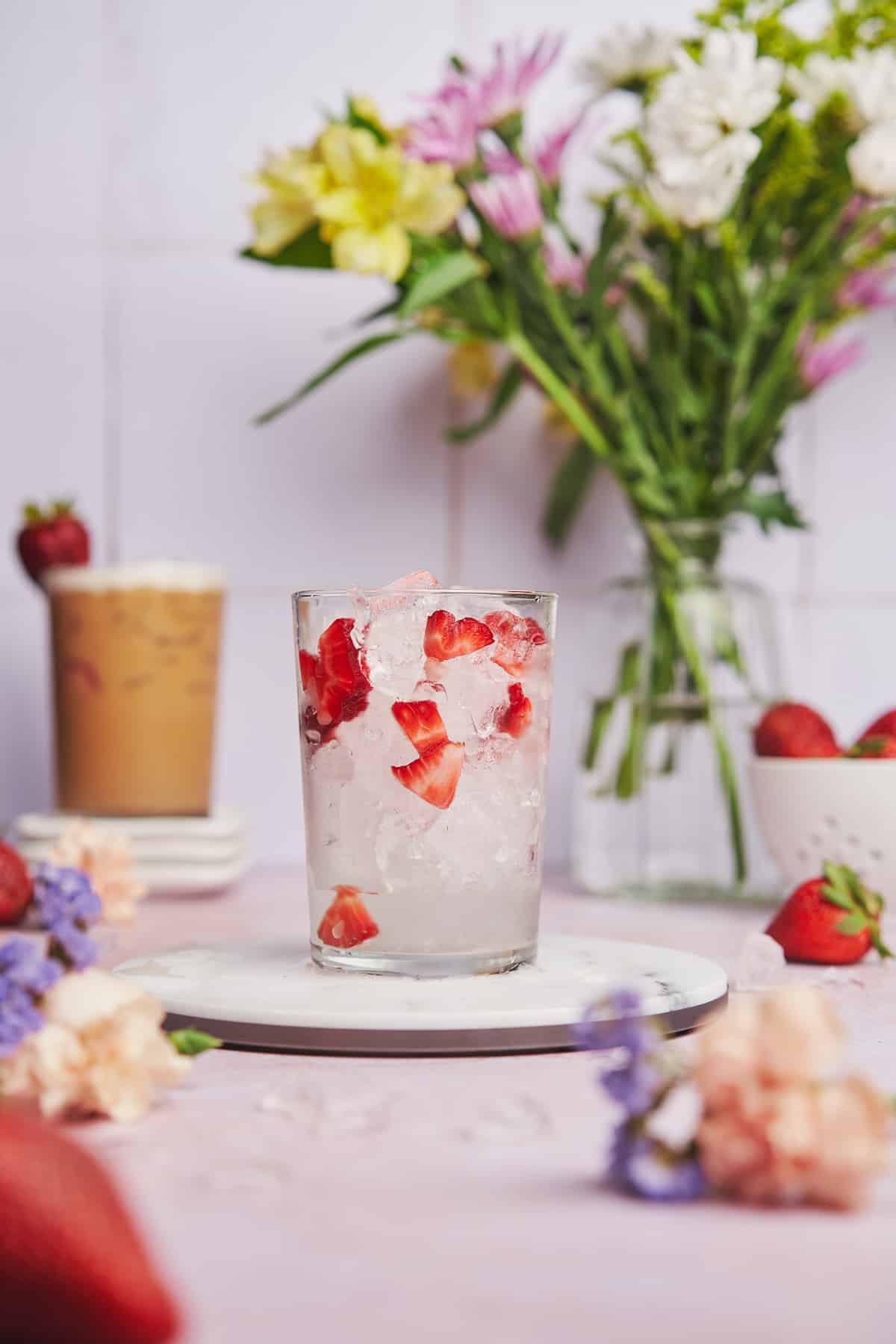 ice and strawberries in a glass with flowers in the background.