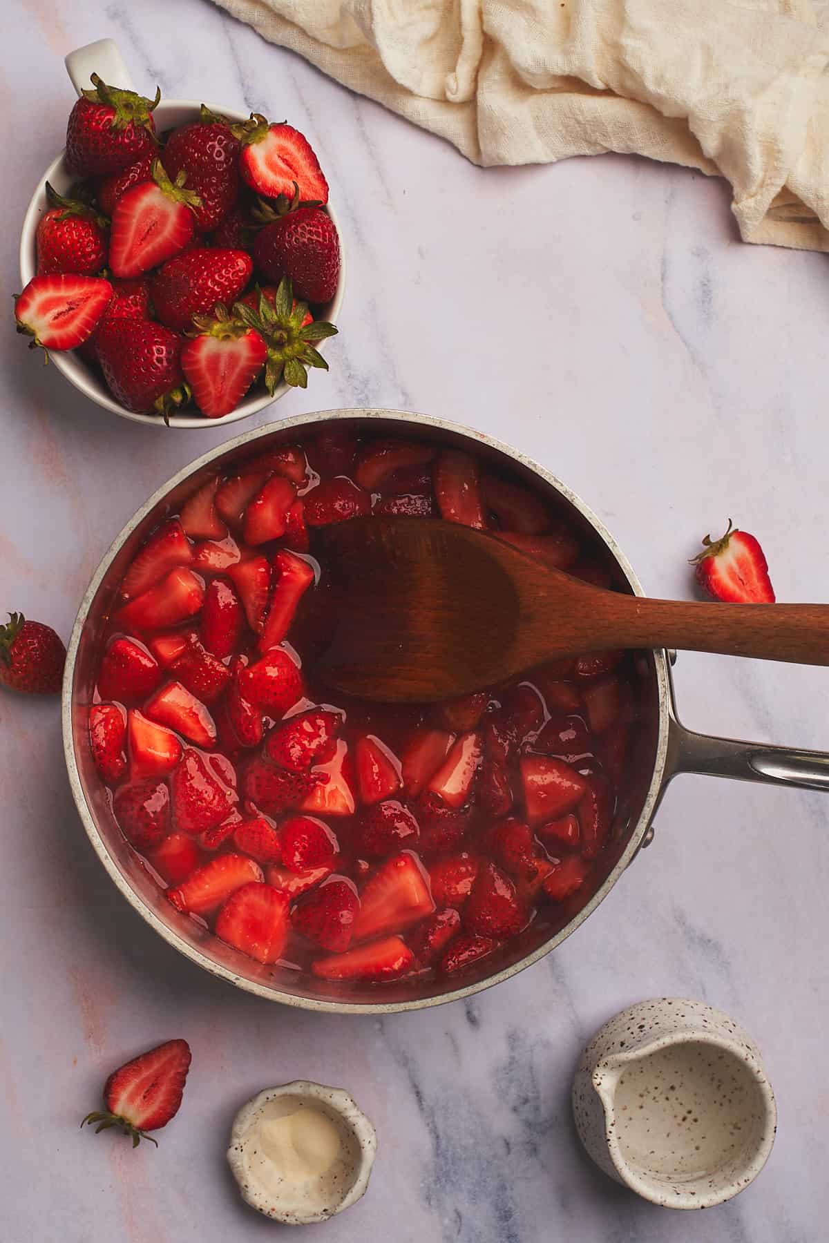 fresh strawberries in a pot with a wooden spoon, and the sweetener dissolved into a liquid sauce. 