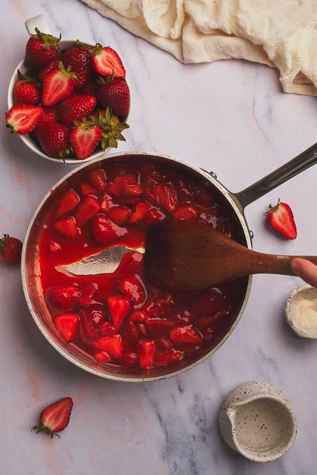 dragging a wooden spoon along the bottom of a saucepan with strawberry sauce to see that the sauce has thickened.