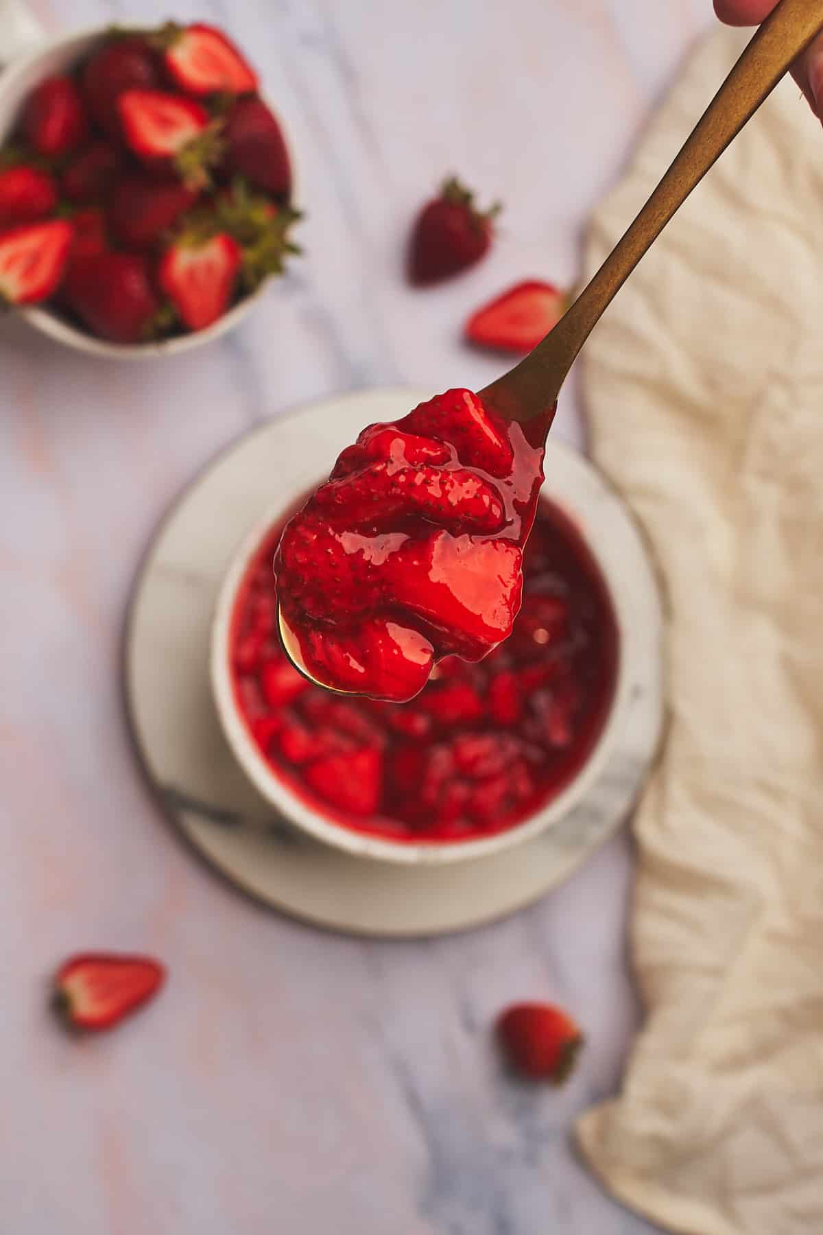 large spoon full of fresh strawberry topping for cheesecake over a bowl of it. 