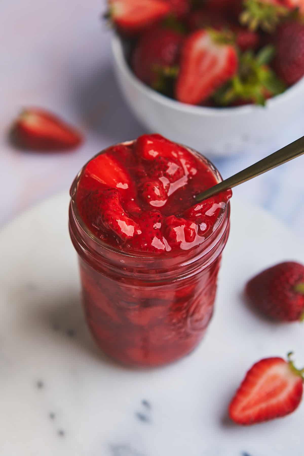 strawberry topping for cheesecake in a small mason jar with a golden spoon in it.