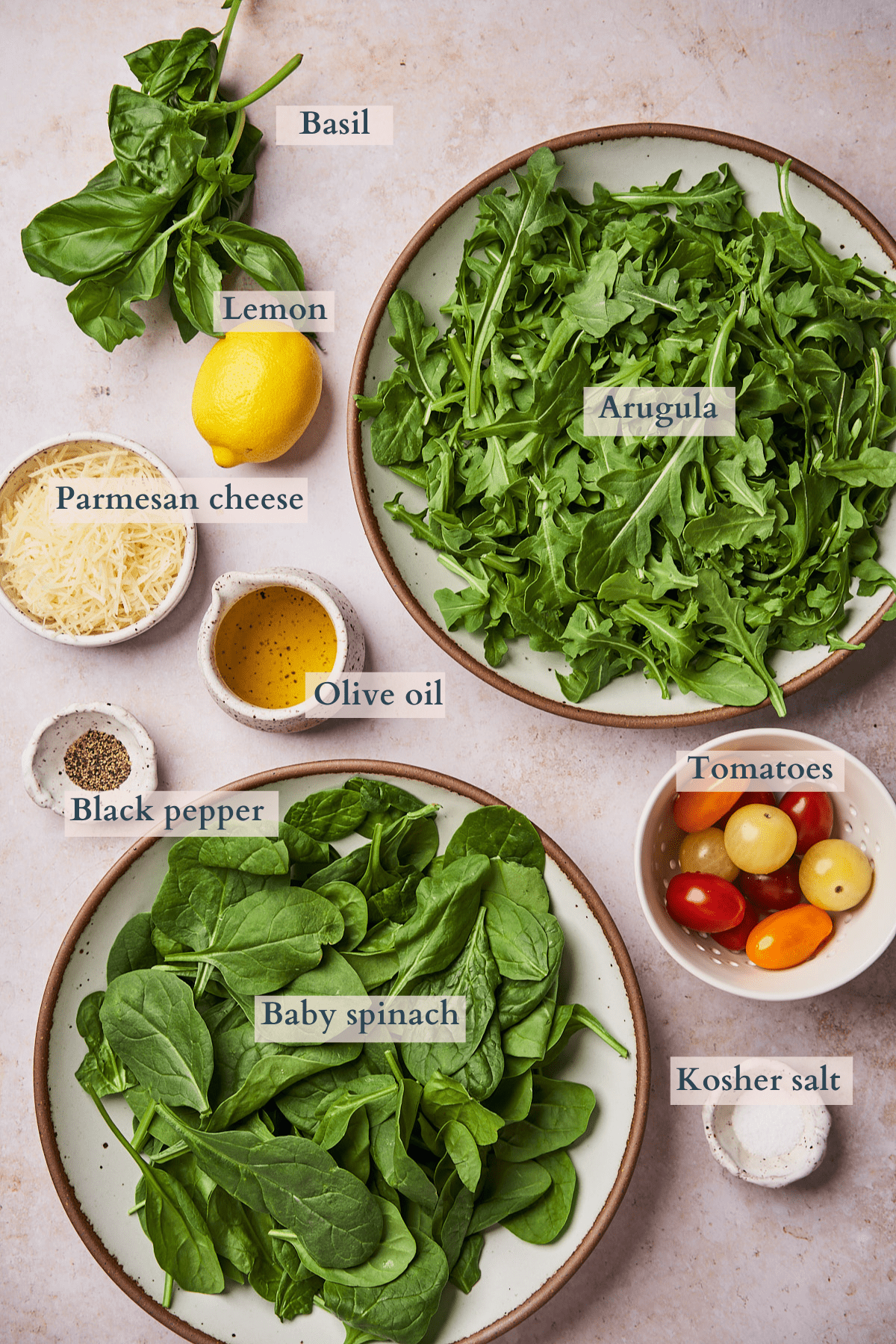 ingredients for arugula spinach salad as a graphic, with text overlaying the ingredients including arugula, spinach, tomatoes, salt, pepper, olive oil, lemon, basil, and parmesan. 