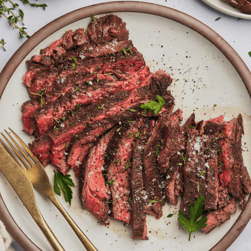 bavette steak recipe on a plate with parsley, thyme, flaky sea salt, and pepper.