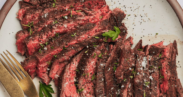 bavette steak recipe on a plate with parsley, thyme, flaky sea salt, and pepper.