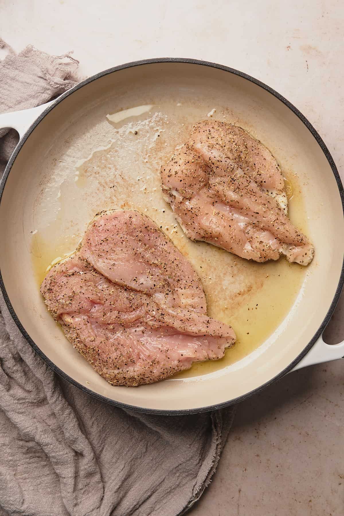 raw chicken breasts seasoned and in a skillet with olive oil.