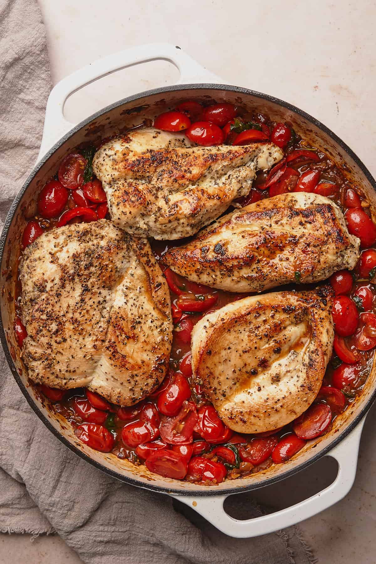 cooked chicken breasts in an enameled cast iron with a fresh tomato sauce underneath. 
