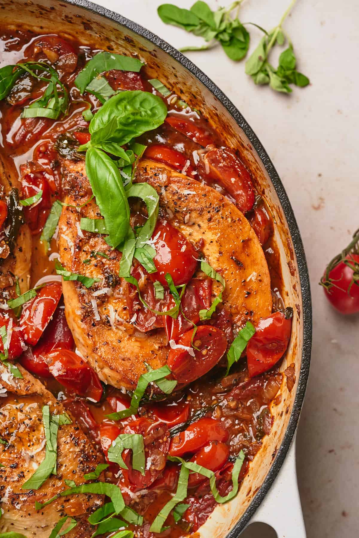 close up shot of chicken covered in tomato sauce and fresh basil in an enameled cast iron skillet. 