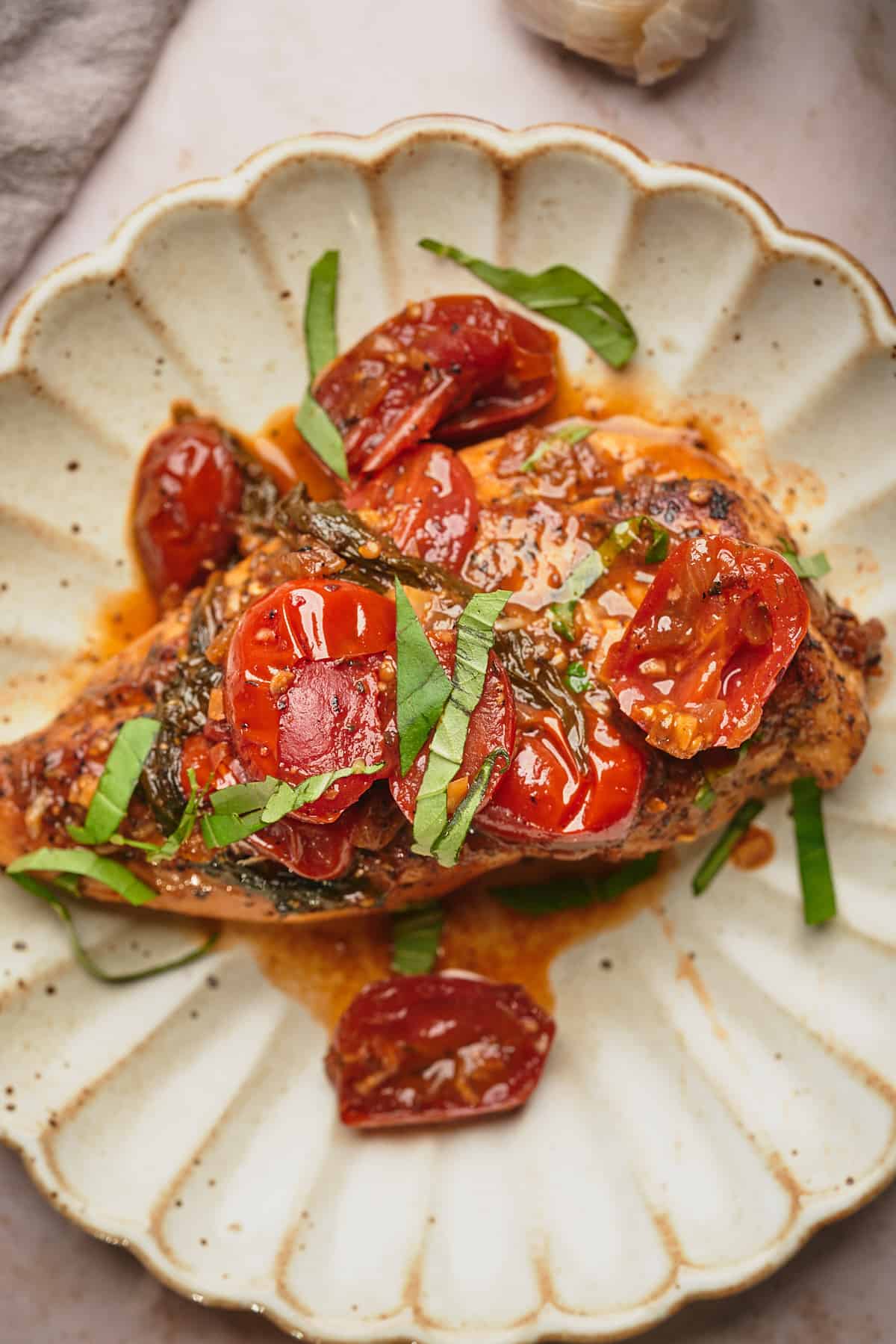 close up shot of a chicken breast topped with cherry tomato sauce, and fresh basil. 