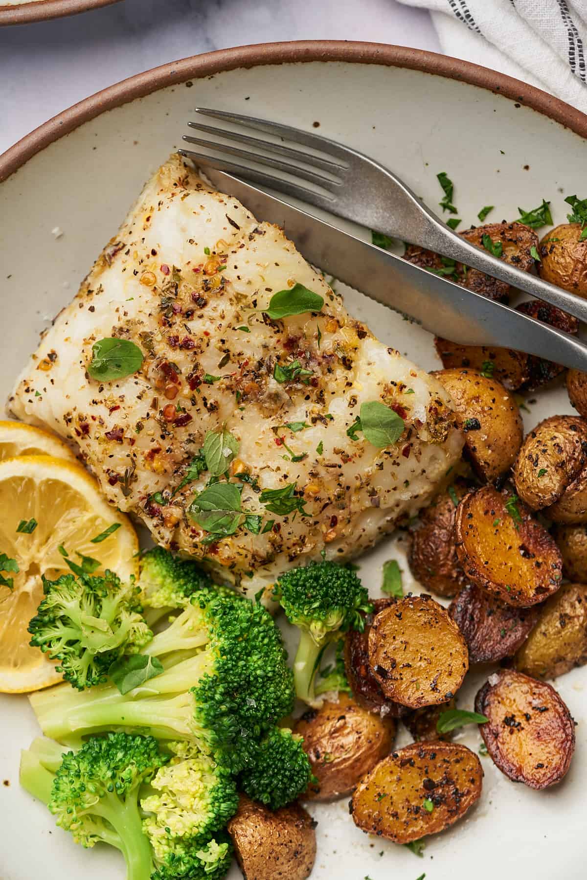 delicious herbed chilean sea bass served with lemon slices, broccoli, and potatoes. 