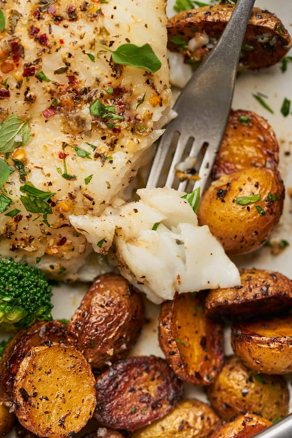 close up shot of flaky chilean sea bass on a fork with roasted potatoes and broccoli. 