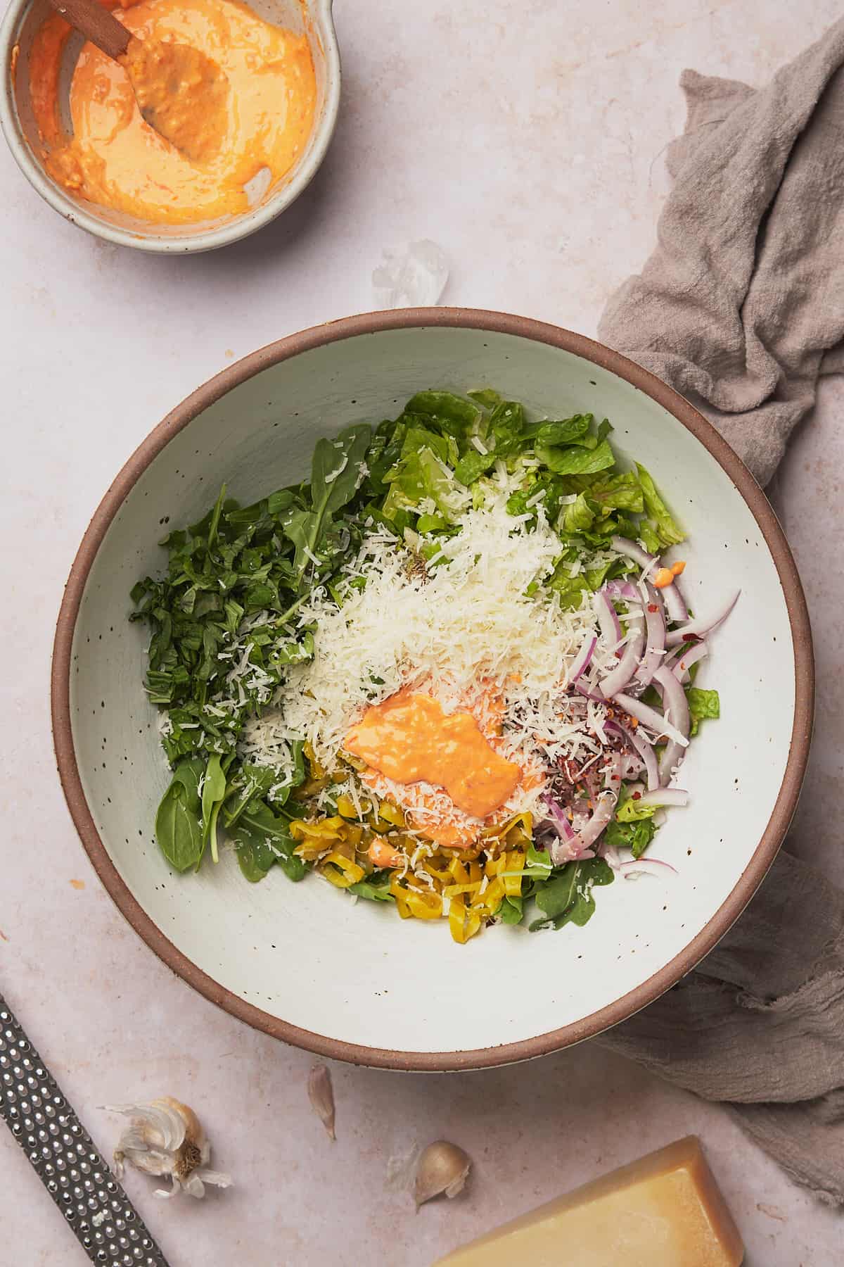 ingredients in a bowl to make an arugula salad with parmesan, chili mayo, and red onions.